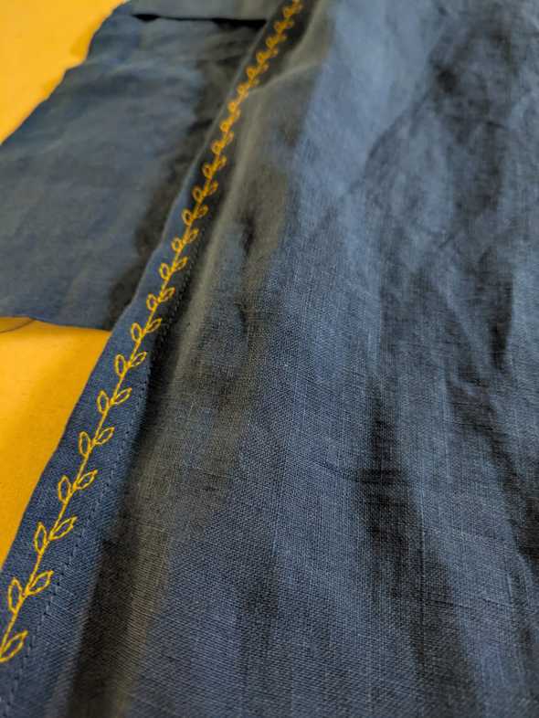 close-up of blue linen fabric with a fancy leaf shaped stitch in yellow thread